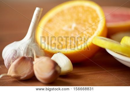 health, food, cooking, traditional medicine and ethnoscience concept - close up of garlic and orange on wooden table