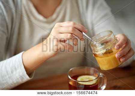health, traditional medicine and ethnoscience concept - close up of woman adding honey to tea with lemon