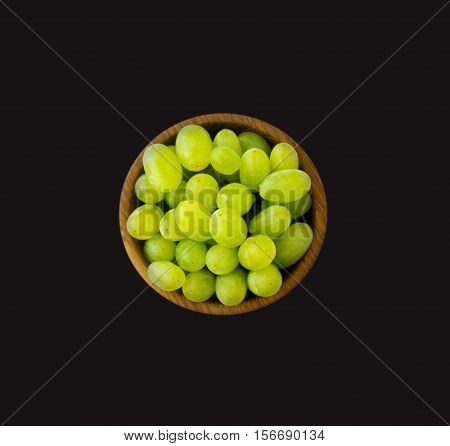 Grapes in a wooden bowl isolated on black background. Green grapes Kish Mish.