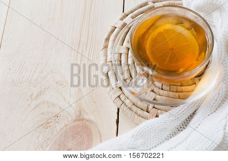 Cozy and soft winter background. Cup of tea with lemon and warm knitted sweater or blanket on a vintage wooden board. Holidays at home. Selective Focus.