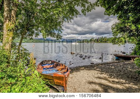Dilapidated rowing boat pulled up onto sandy shore of Lake Windermere in the English Lake District, Cumbria.
