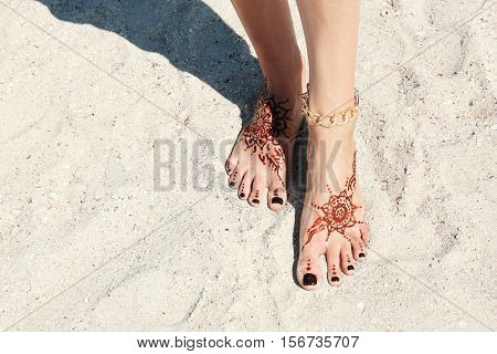 Female legs with henna tattoo on beach sand background