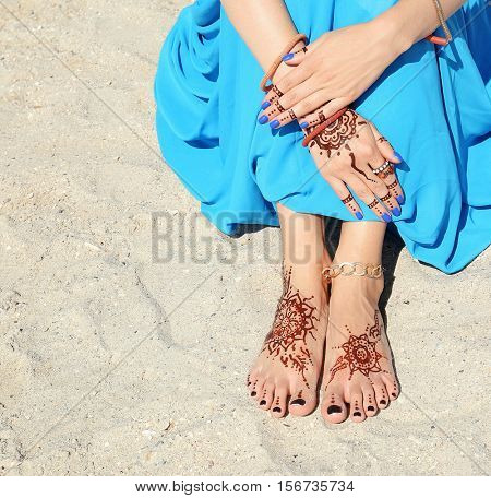 Female legs and hands with henna tattoo on beach sand background