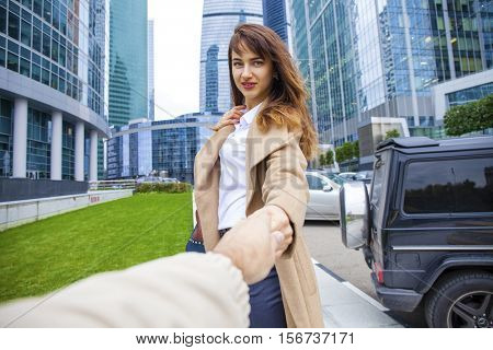 Follow Me. Young beautiful woman in beige coat drags her boyfriend, autumn streen outdoors