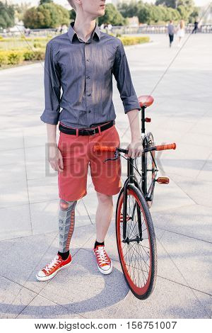 Hipster with red bycicle and tattoo on leg.