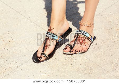 Female legs with henna tattoo on beach sand background