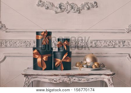 Wrapped gift black boxes with ribbons as Christmas presents on a table on luxury white wall design bas-relief stucco mouldings roccoco elements.