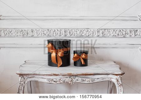 Wrapped gift black boxes with ribbons as Christmas presents on a table on luxury white wall design bas-relief stucco mouldings roccoco elements.