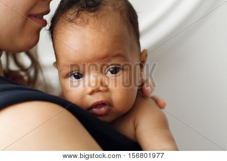 Adorable cute african newborn baby portrait. Little kid looking at camera while mother holding him in carrier, close-up