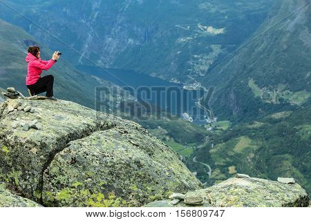 Tourism vacation and travel. Female tourist taking photo with camera enjoying Geiranger fjord and mountains landscape from Dalsnibba Plateau viewpoint Norway Scandinavia.