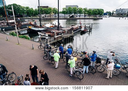 Amsterdam Netherlands - August 1 2016: People riding bicycles in the pier with old sailing ships in Amsterdam. High angle view.