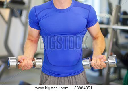 Young man does exercises with dumbbells in modern gym, noface, shallow dof