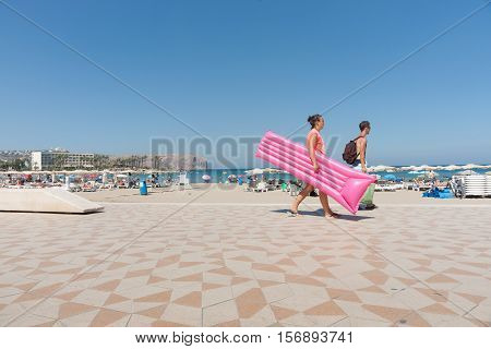 Xabia, Spain - September 7, 2016: Young couple on warm summer clear day walk anlong beautiful beach carrying  pink inflatable lilo float on Mediterranean Costa Blanca Spain