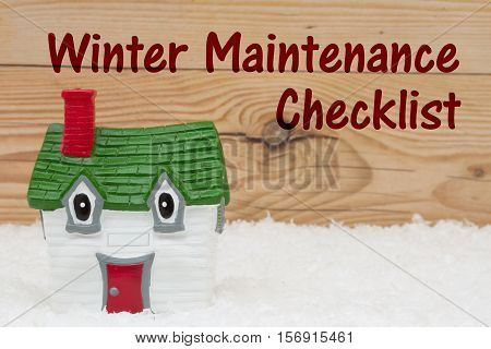 Your house in the winter season A green and red house on snow and a weathered wood background with text Winter Maintenance Checklist