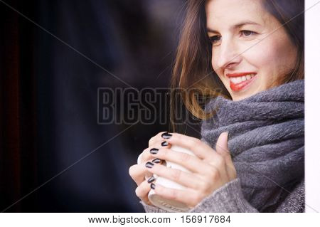 attractive adult woman drinking coffee and looking out of the window on cold day, close up portre in winter time