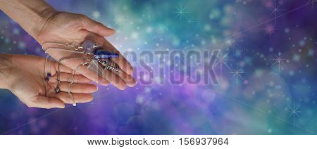 Choose a dowsing pendulum that resonates with you - Female dowsing practitioner holding four radionics pendants in an offering gesture on a wide blue green ethereal  background with copy space