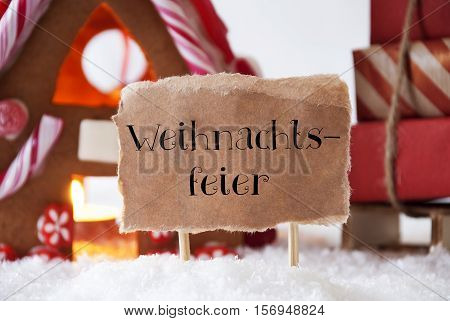 Label With German Text Weihnachtsfeier Means Christmas Party. Gingerbread House In Snowy Scenery As Christmas Decoration. Sleigh With Christmas Gifts Or Presents.
