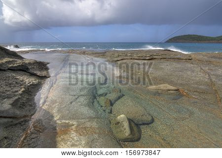Shallow tide pool on rocky northeast shore of Isla Culebra at lowtide as gray clouds drop rain over the sea