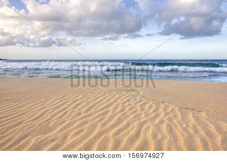 Wide angle closeup of ripples in coarse orange sand as waves roll into shore on Playa Brava on Isla Culebra in Caribbean Sea under diffused natural light