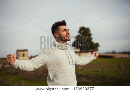 Strong guy open his arms in the meadow. 