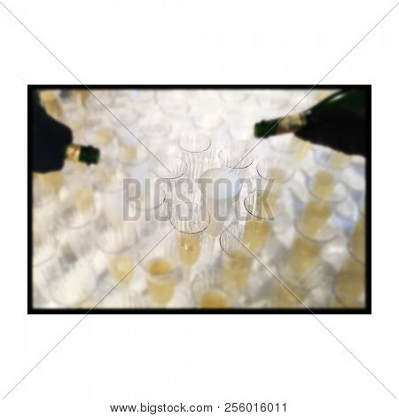 Two bottles of champagne being poured at the same time into dozens of plastic glasses on a table at a festive party.