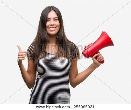 Young hispanic woman holding megaphone happy with big smile doing ok sign, thumb up with fingers, excellent sign