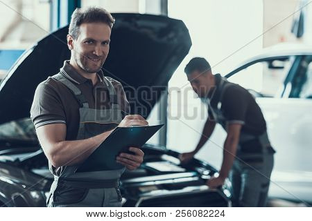 Two Handsome Happy Auto Mecanics In Garage. Portrait Of Attractive Repairmen In Grey Uniform Showing