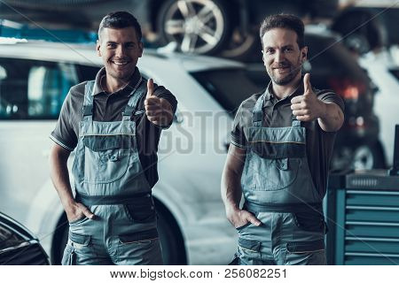 Two Handsome Happy Auto Mecanics Keeping Thumbs Up. Excited Attractive Repairmen In Grey Uniform Sho