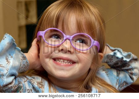 A Young Girl With Strabismus Tries On New, Pink Glasses Frames On.  She Is Looking Up And To The Sid