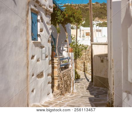 Beautiful narrow street with white houses in Mikonas island, Greece. Traditional narrow street with white facedes of buildings and blue doors