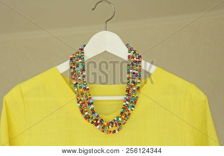 Bright Beads Of Murano Glass Hang On The Background Of A Yellow Summer Dress. Summer Jewelry, Summer