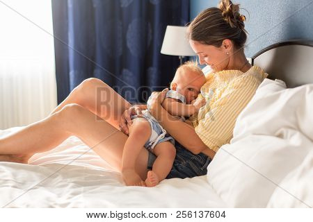 Young Mother, Sitting In Bed With Her Baby Boy, Having Shared Moment Of Joy, Breastfeeding, Hugging,