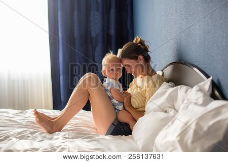 Young Mother, Sitting In Bed With Her Baby Boy, Having Shared Moment Of Joy, Breastfeeding, Hugging,