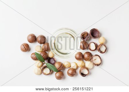 Cosmetic Macadamia Oil And Heap Of Nuts On White Table From Above.