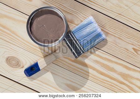 Blanched Pine Boards Ready For Painting In Brown Color, A Brush With Blue Bristles And A Can Of Pain