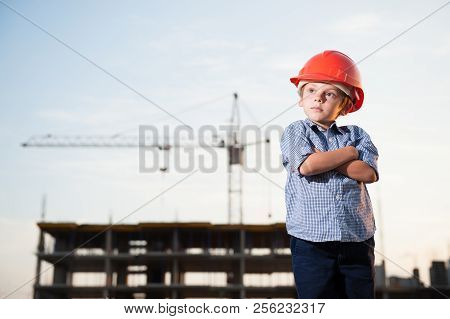 Handsome American Caucasian Kid In Orange Helmet On Construction Site With High Crane