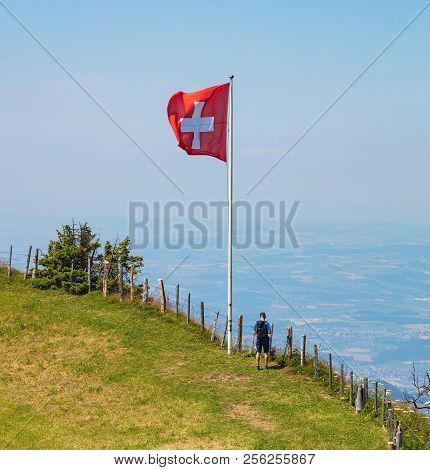 Mt. Rigi, Switzerland - July 19, 2018: A Person Standing At A Flag Of Switzerland On Mt. Rigi. The R