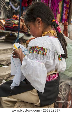 Otavalo, Ecuador - August 4, 2012: Indian Girl In National Clothes Sells The Products Of Her Weaving