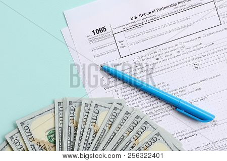 1065 Tax Form Lies Near Hundred Dollar Bills And Blue Pen On A Light Blue Background. Us Return For 