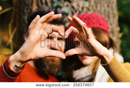 Couple In Love Shows Heart Sign With Fingers. Man And Woman With Blured Faces On Tree Background. Gi