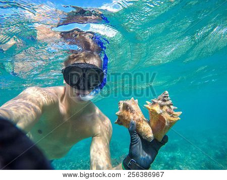 Underwater Wide Angle Selfie Of Muscular Freediver With Two Shell