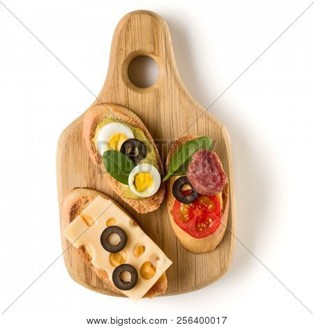 Open faced sandwich canape or crostini on a wooden serving board isolated on white background closeup. Top view.
