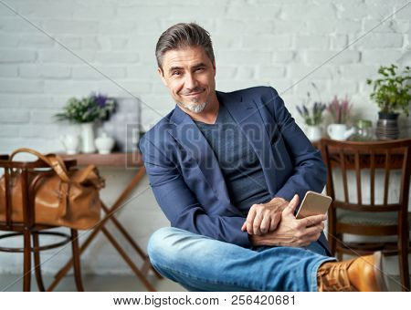 Portrait of happy older white man with gray hair wearing jacket smiling holding smart phone. 
 .