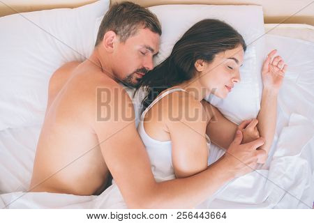 Gorgeous Couple Is Lying In Bed Together. They Sleep. Guy Is Lying Behind Girl. He Holds His Hand On