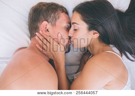 Close Up Of Guy And Girl Lying In Bed And Kissing. She Touches His Head With Hand. They Are Lying On
