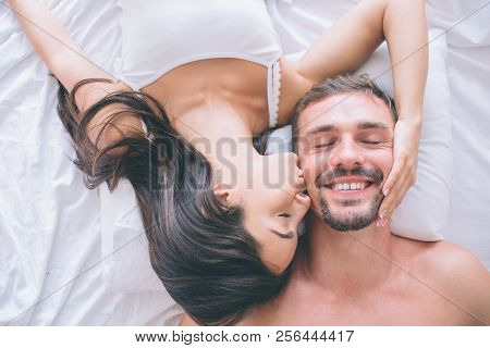 Gorgeous And Attractive Couple Is Lying In Bed Face To Face. Guy Keeps His Eyes Closed And Smiles. G
