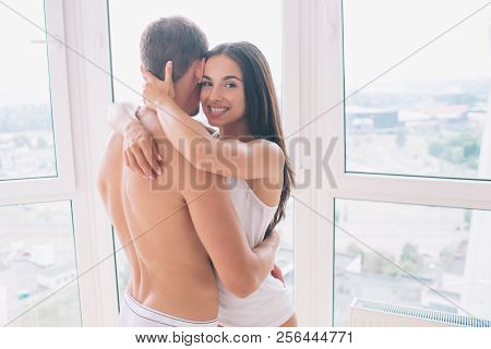 Cherful Girl Stands With Guy And Embraces Him. She Looks On Camera And Smiles. Guy Holds His Hands O