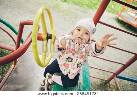 A Ittle Girl Playing In The Playground. Children's Hand Holding The Steering Wheel