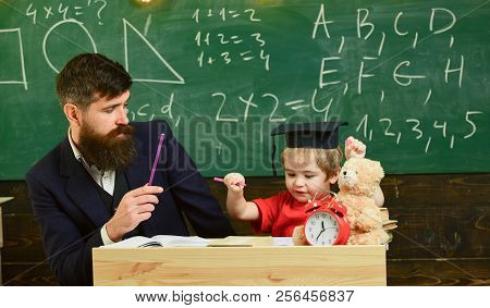 Schoolboy Doing Hometask With Father And Writting In Workbook, Chalkboard On Background. Father Chec
