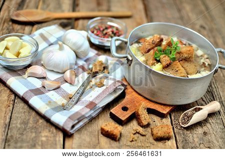 Garlic Soup In An Old Saucepan, Fresh Garlic Bulbs, Cloves, Colored Pepper, Wooden Spoon, Croutons A